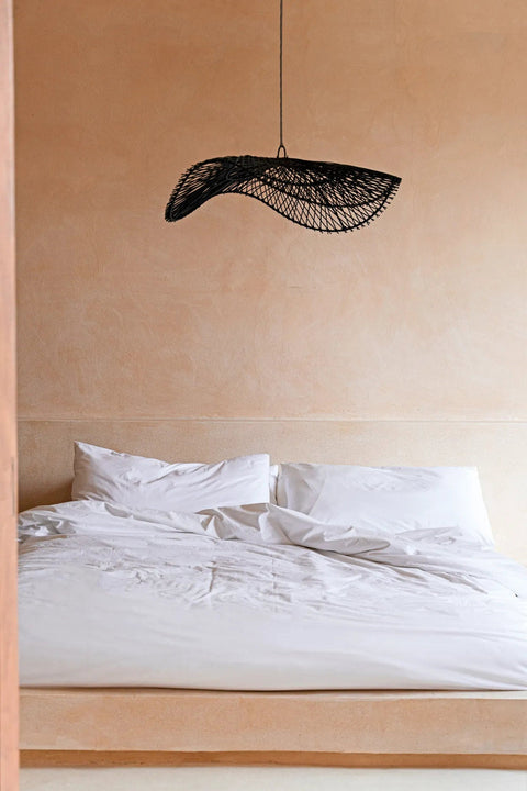 Zwarte rotan lamp The Chapeau boven bed in bohemian slaapkamer.