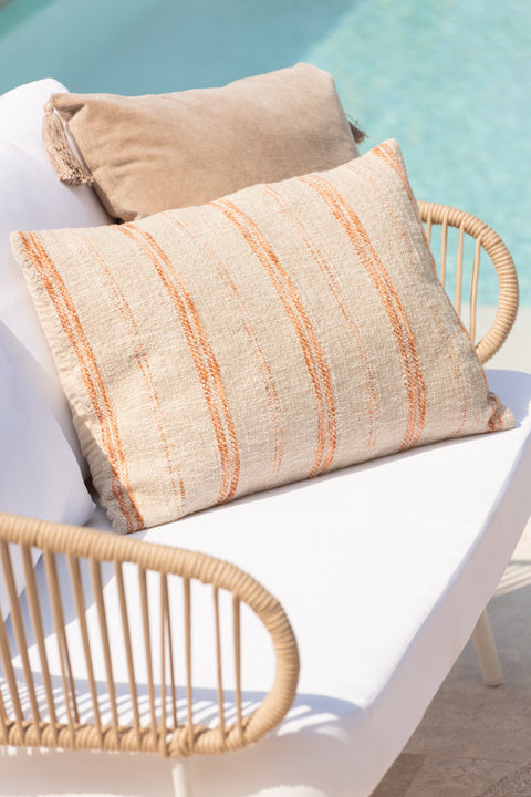 Langwerpig J-Line kussen ‘Linen Orange’ in rotan zetel met ander kussen, met uitzicht op zwembad in zomerse setting.