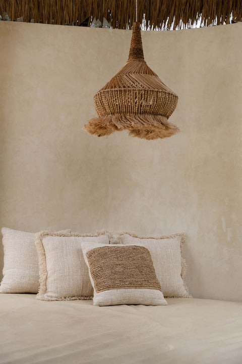 Kussen ‘Raffia Stamp’ als decoratief accent op een wit bed in serene slaapkamer
