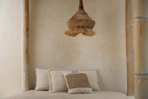 Boho kussen met raffia opgemaakt op bed naast lichte plaids en linnen dekbedovertrek