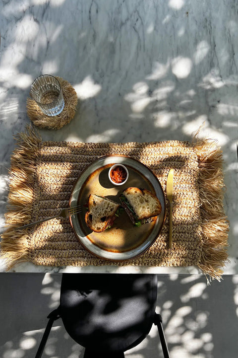 Raffia placemat met bord op schaduwrijk terras – boho tafeldecoratie