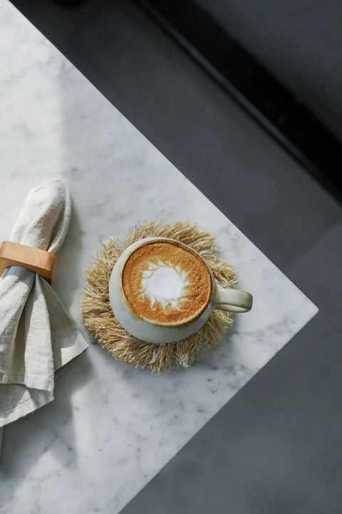 Serviettenring 'Teak Root' rond servet bij tas met koffie op rotan onderlegger