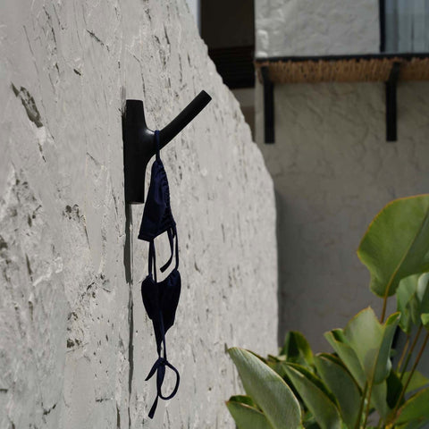 Zwarte kapstokhaak aan een witte buitenmuur met een bikini eraan