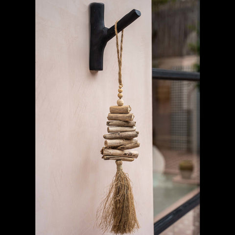 Zwarte kapstokhaak tegen een beige buitenmuur met een decoratieve rotan hanger