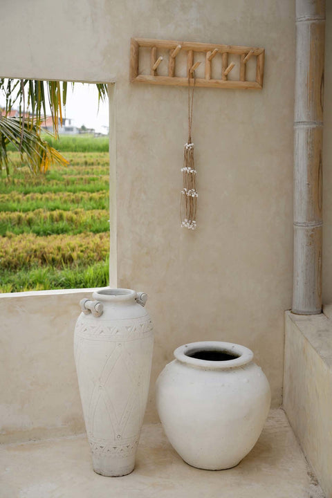 Teakhouten kapstok met decoratieve schelpenketting aan een beige muur boven twee grote witte vazen