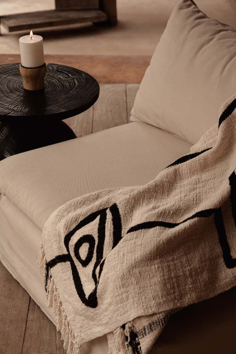 Bazar Bizar The Evil Eye plaid over een beige zetel naast een bruin houten bijzettafeltje.