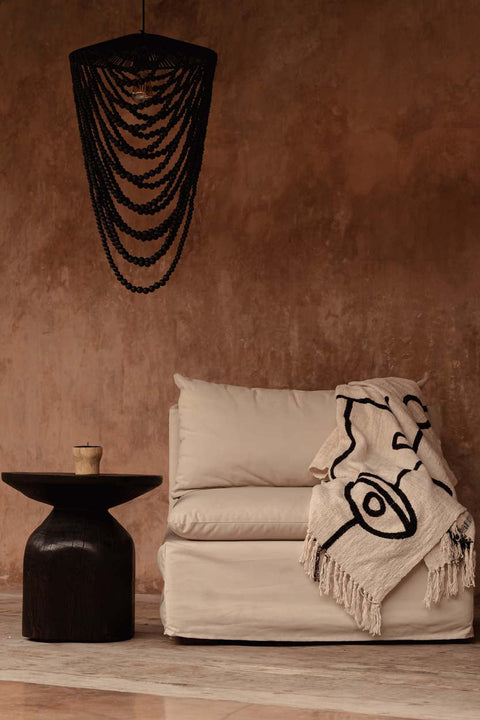 Bazar Bizar The Evil Eye plaid gedrapeerd over een beige zetel tegen een warme bruine muur.