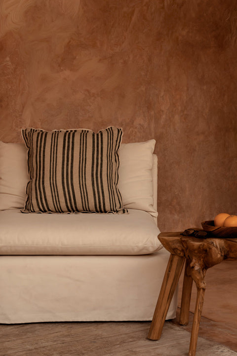 Bazar Bizar The Nordic Stripe kussen op een beige zetel tegen een bruine muur in een warm interieur.