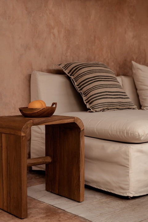 Bazar Bizar The Nordic Stripe kussen op een beige zetel naast een houten bijzettafeltje.