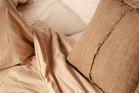 Bazar Bizar The Sahara Fringe kussen op een beige zetel gecombineerd met een zacht bruin plaid.