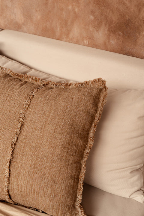 Bazar Bizar The Sahara Fringe kussen op een beige zetel tegen een warme bruine muur.