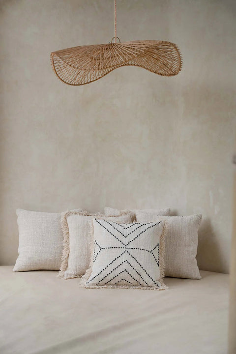 Bazar Bizar The Tribal kussen gecombineerd met andere sierkussens op een bed onder een rotan hanglamp.