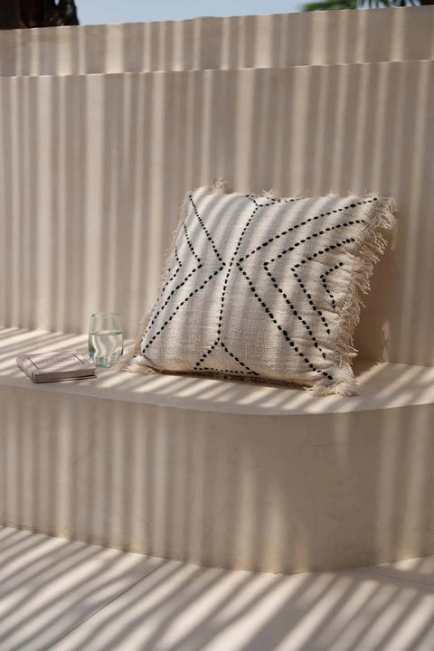 Bazar Bizar The Tribal kussen gestyled op een beige buitenbank tegen een lichte muur voor een warme, natuurlijke sfeer.