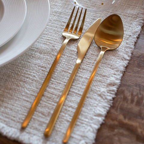 J-Line bestekset Matt Gold op een beige tafelkleed naast een bord.