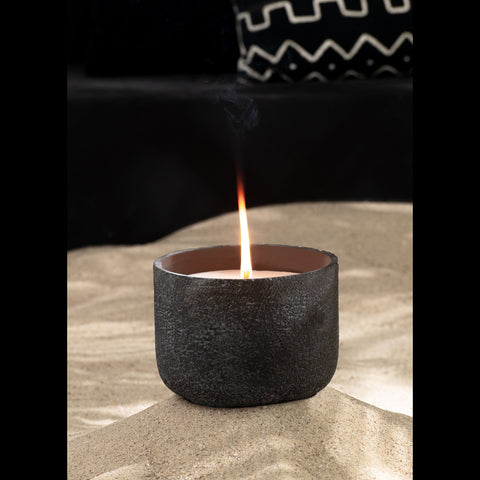 Brandende J-Line buitenkaars Round Dark Grey small op zand met zwarte bank op achtergrond