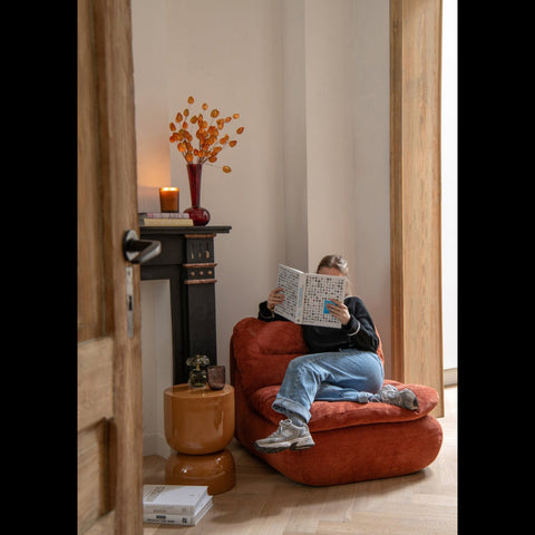 J-Line Foam loungestoel in roestbruin in een sfeervol interieur met vrouw die boek leest