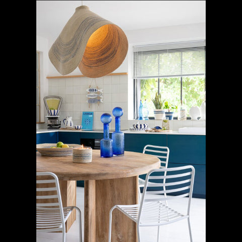 J-Line Striped Seagrass hanglamp boven een houten eettafel met blauwe glazen flessen als decoratie