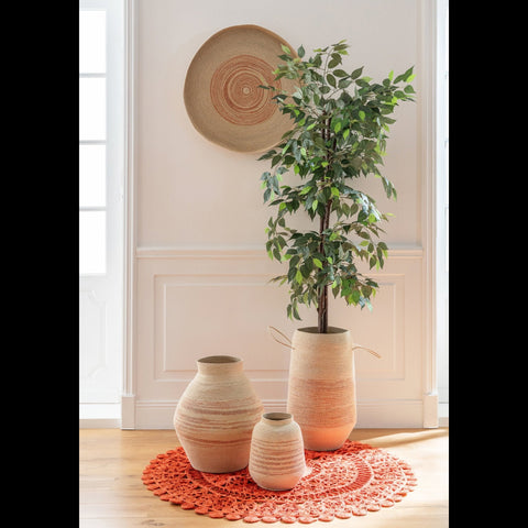 Naturel mand met oranje strepen gecombineerd met bijpassende manden, waaronder een mand met groene plant, op een ronde oranje mat in een beige interieur