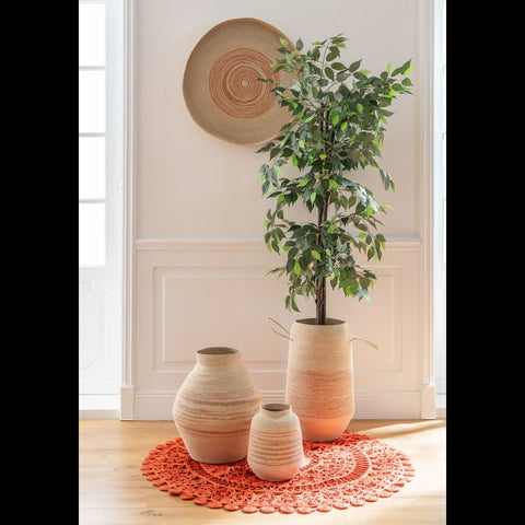 Naturel zeegrasmand met oranje strepen gecombineerd met bijpassende manden, waaronder een mand met groene plant, op een ronde oranje mat in een beige interieur
