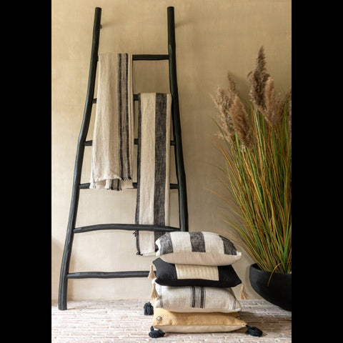 Zwarte teakhouten ladder met plaids, kussens en een groene plant tegen een beige muur