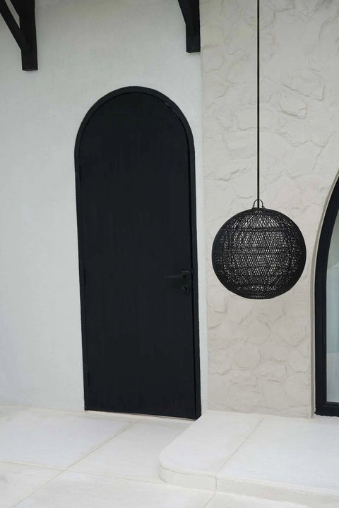 Zwarte rotan lamp The Bubble medium naast zwarte deur buiten.