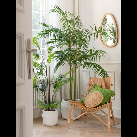 J-Line Spiegel Paille Medium tegen een beige muur boven een houten rotan stoel met grote kamerplanten