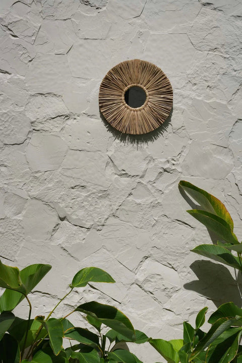 The Alang Alang Large spiegel gestyled tegen een beige buitenmuur