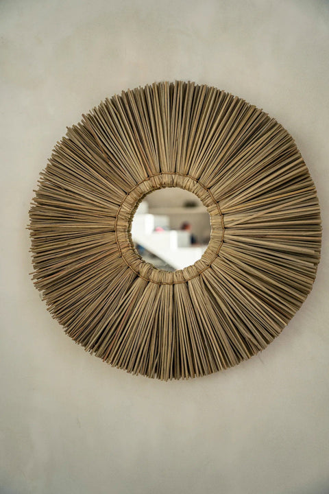 Ronde Alang Alang Large spiegel tegen een beige muur in een bohemian interieur