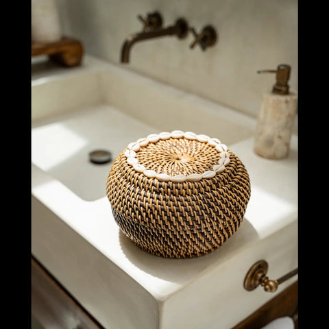 Bruine rotan mand The Colonial Peek-a-Boo met kaurischelpen op een wastafel in de badkamer